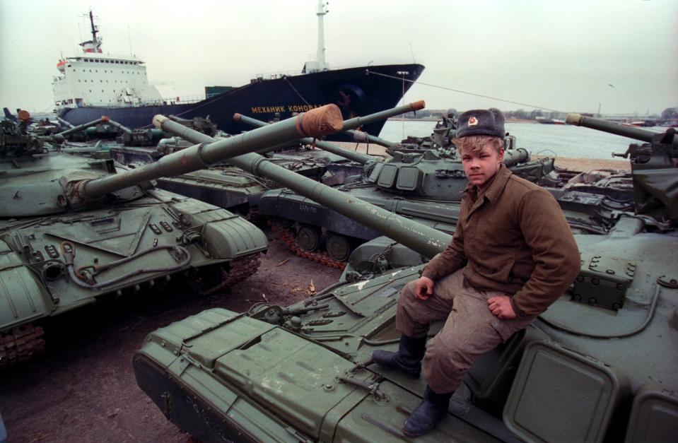 A Soviet soldier sits on one of many tanks next to a ship.