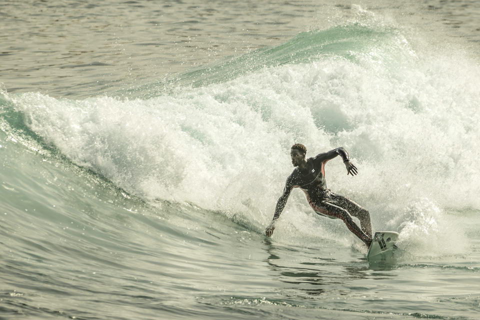 Cherif Fall, Senegal's number one surfer paddles to the wave in the Atlantic Ocean in Dakar, Senegal, Wednesday, Feb. 28, 2024. Instead of training in the waves off his Senegal homeland, Fall was wistfully preferring to be in Puerto Rico, where the last surfing qualifying competition for the Paris Olympics ends on Saturday. Senegal had nobody there to try and claim the last 14 spots for men and women because there was no money to send them, Fall says. (AP Photo/Sylvain Cherkaoui)