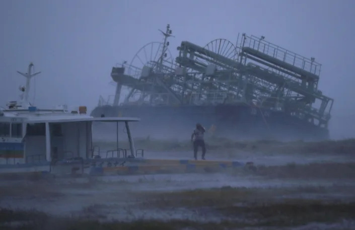 A person stands looking at a ship that was washed ashore by a typhoon.