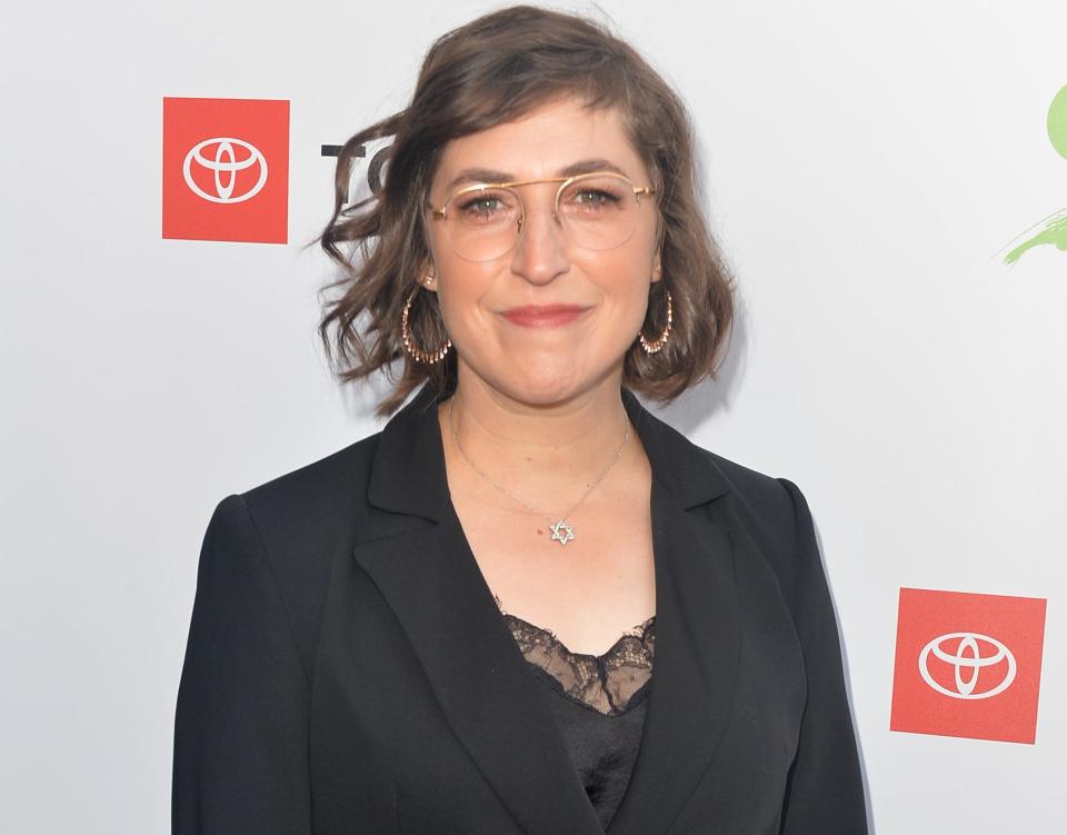 Mayim wears glasses and a suit jacket at an event