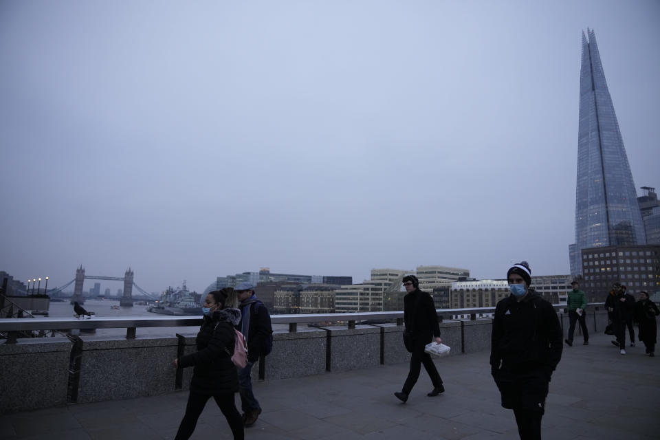 Workers walk over London Bridge towards the City of London financial district, backdropped by Tower Bridge and the Shard, Britain's tallest skyscraper, during the morning rush hour, in London, Monday, Jan. 24, 2022. The British government have asked people to return to working in offices starting Monday as they ease coronavirus restrictions. (AP Photo/Matt Dunham)