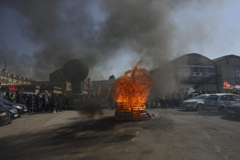 Demonstrators stand next to burning pallets as they stage a protest against the pension reforms at Gare de Lyon train station in Paris, Thursday, April 20, 2023. Union activists stage scattered actions to press France's government to scrap the new law raising the retirement age. (AP Photo/Thibault Camus)