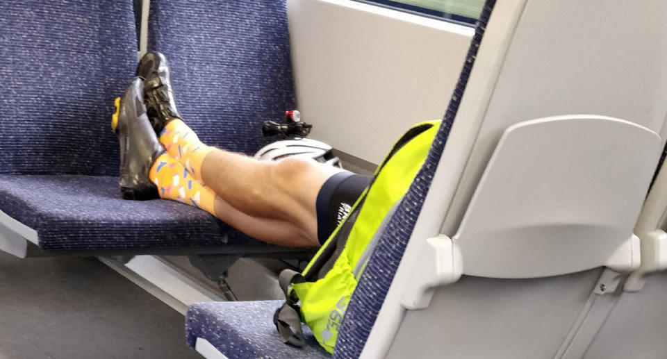Photo of cyclist taking up four seats on a train with his feet and belongings.