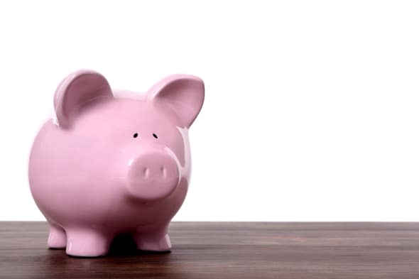 Traditional pink piggy bank standing on a wood table or shelf. Space for copy.