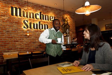 Michael Abbey, from Sierra Leone, serves coffee to his boss Kathrin Wickenhaeuser while working as waiter in a restaurant called 'Muenchner Stuben' in Munich, Germany, October 12, 2015. REUTERS/Michaela Rehle