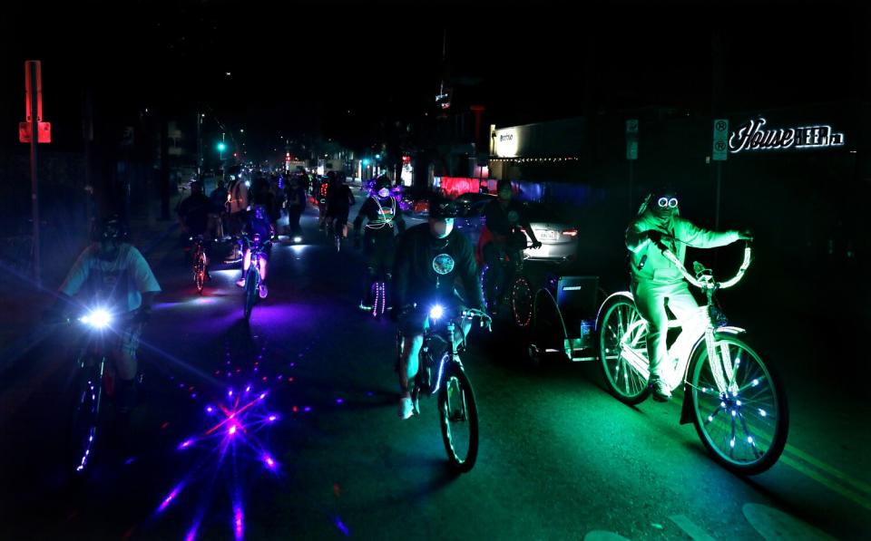 A group of cyclists riding illuminated bikes at night.