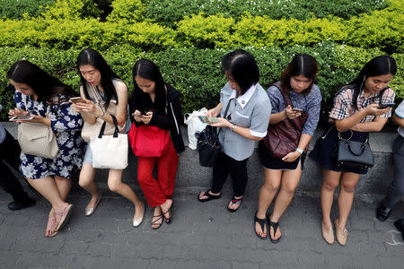 Women use their mobile phones while waiting for a bus at rush hour in Bangkok, Thailand October 4, 2018. REUTERS/Jorge Silva