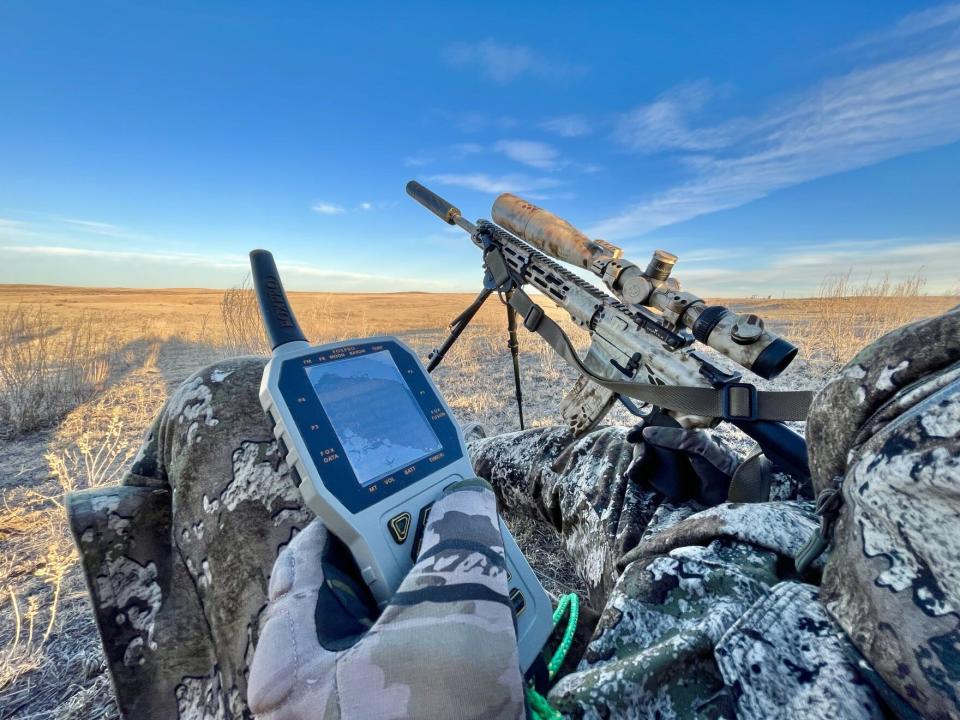 Bryan Garrison holds the remote that controls his electronic coyote calling machine. He's equipped with two firearms: a 12-gauge shotgun and the 224 suppressed rifle seen here.