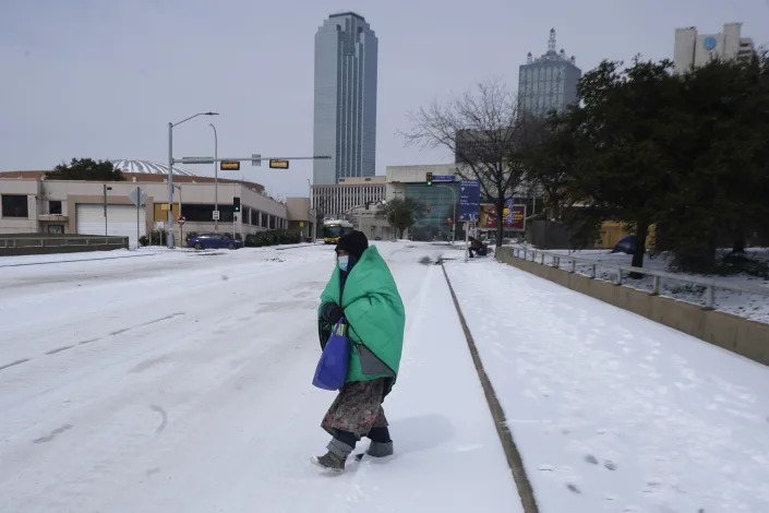 A woman wrapped in a blanket crosses the street near downtown Dallas, Tuesday, Feb. 16, 2021. Temperatures dropped into the single digits as snow shut down air travel and grocery stores. (AP Photo/LM Otero)
