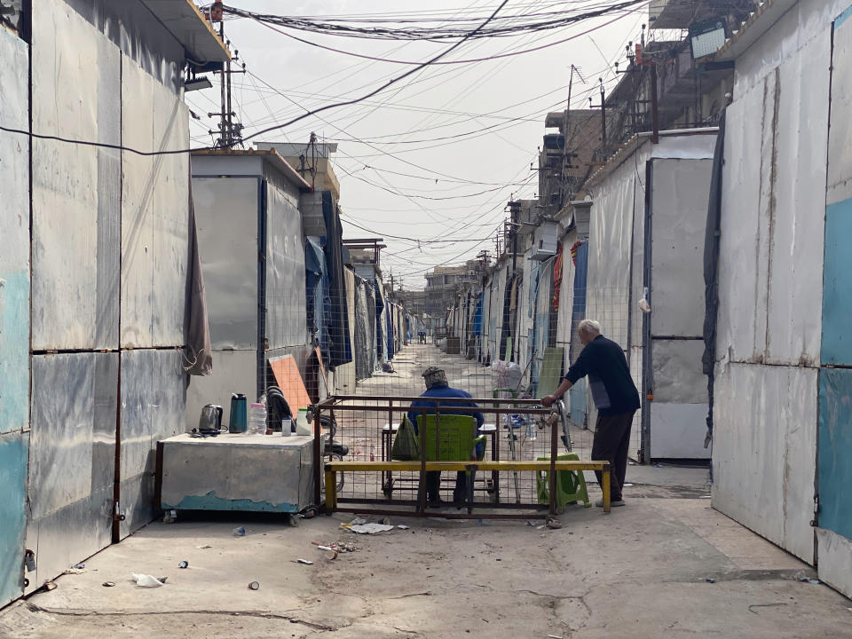 People sit near shops that are shuttered to help prevent the spread of the coronavirus during a curfew at a nearly empty popular market in the eastern suburb of Baghdad, Iraq, Wednesday, April 8, 2020. (AP Photo/Khalid Mohammed)