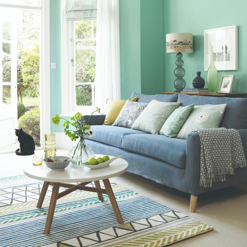 A green-painted living room with a blue sofa with storage behind it displaying a table lamp and decorative objects