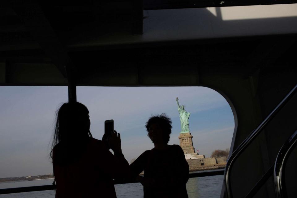 PHOTO: Tourists pose for pictures as the cruise goes around the statue of Liberty, Jan. 21, 2018 in New York. The iconic landmark closed as part of the US government shutdown in 2018. (Eduardo Munoz Alvarez/Getty Images, FILE)
