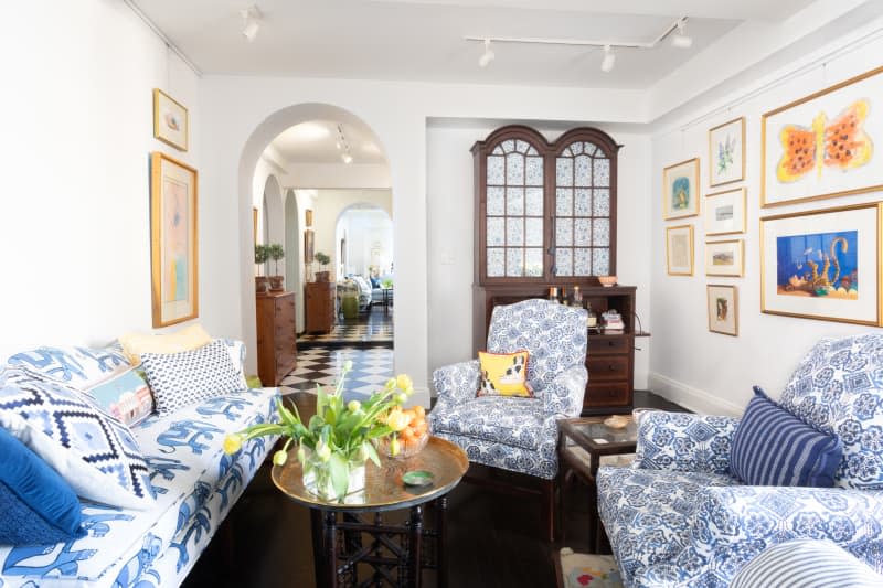 Living room with blue and white patterned sofa and accent chairs, white walls, dark wood floor and antique cabinet that also works as a bar cart