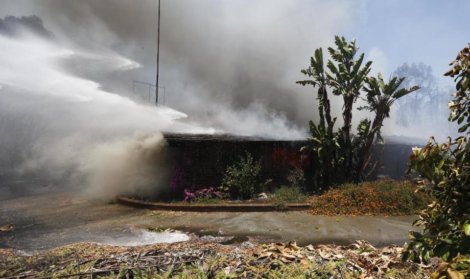 Agua y humo sobre una casa quemada por un incendio forestal el miércoles 14 de mayo de 2014 en Carlsbad, California. Las llamas impulsadas por el viento amenazan las casas en la ciudad costera de Carlsbad, donde las autoridades enviaron avisos para evacuar más de 11.000 casas y establecimientos. (Foto AP Photo)