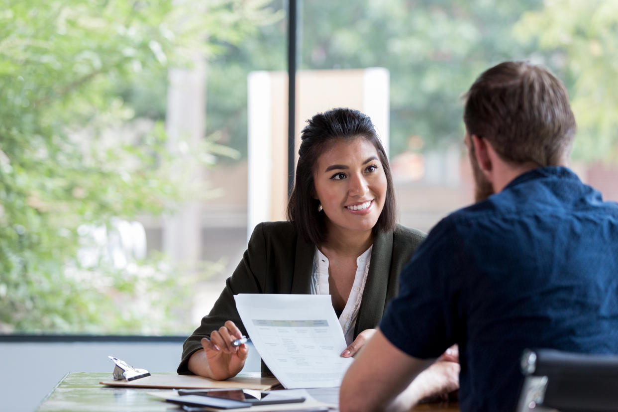 Hispanic businesswoman smiles while showing a document to a male associate.