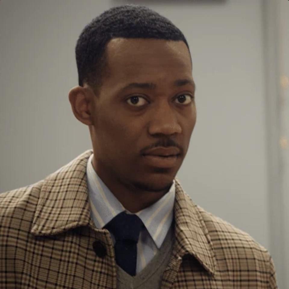 Tyler James Williams dressed in a plaid jacket, blue shirt, and tie looks into the camera