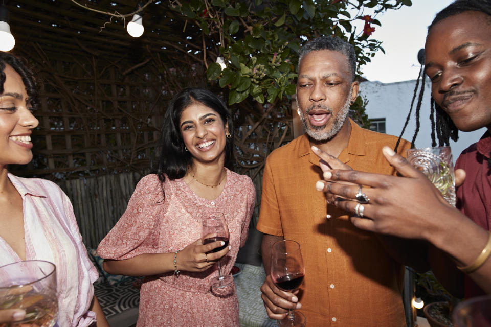 People at a social gathering with drinks; two women and two men smiling and conversing in an outdoor setting