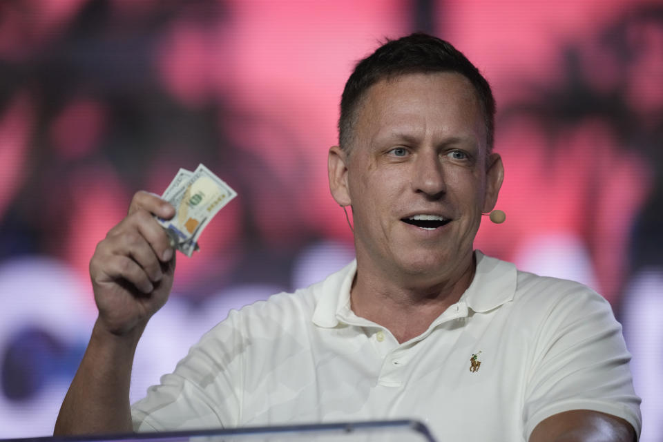FILE - Peter Thiel, co-founder of PayPal and Palantir, offers a pair of hundred dollar bills to attendees during a keynote address at the Bitcoin Conference, April 7, 2022, in Miami Beach, Fla. Millionaire candidates and billionaire investors are harnessing their considerable personal wealth to try to win competitive Republican primaries for open U.S. Senate seats in Ohio and Pennsylvania. Billionaire tech investor Thiel has poured money into a super PAC backing “Hillbilly Elegy” author JD Vance. (AP Photo/Rebecca Blackwell, File)