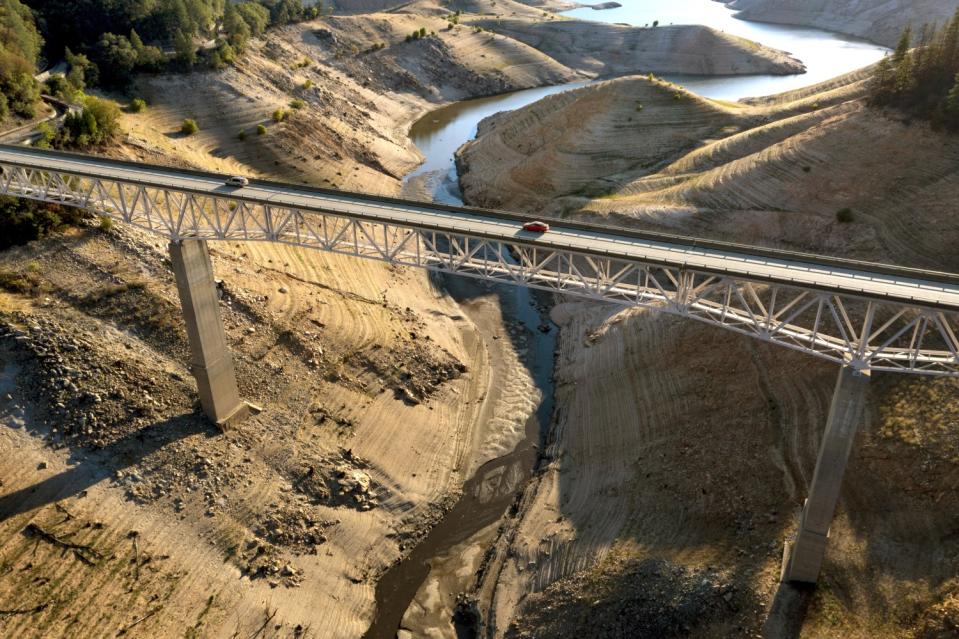 Vehicles cross a bridge across a nearly dry arm of a lake