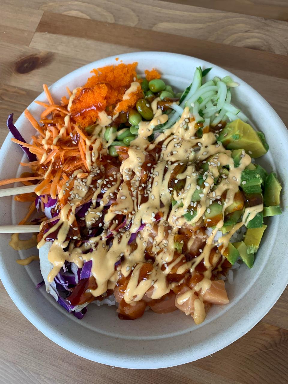 A build-your-own poke bowl at Poke & Roll features rice, spicy salmon, cucumber, carrot, edamame, red cabbage and avocado. Toppings are spicy mayor, Gochujiang sauce, toasted sesame seeds, masago (fish roe) and sushi ginger.