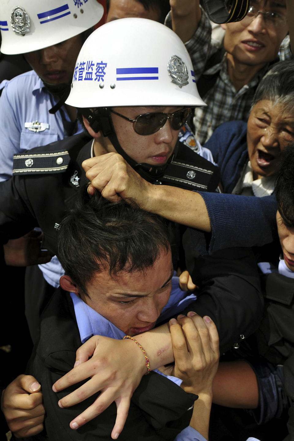 In this Aug. 12, 2008 photo, an officer of the urban management bureau, known as chengguan in Chinese, center, protects his colleague, bottom, who allegedly beat up four street vendors, from an angry mob at a market in Kunming, in southwestern China's Yunnan province. The urban management bureau, a branch of city governments that China set up to monitor everything from unlicensed street vendors to unauthorized construction, is rife with abuse of power, stoking already high social tensions, a rights group said Wednesday. (AP Photo) CHINA OUT