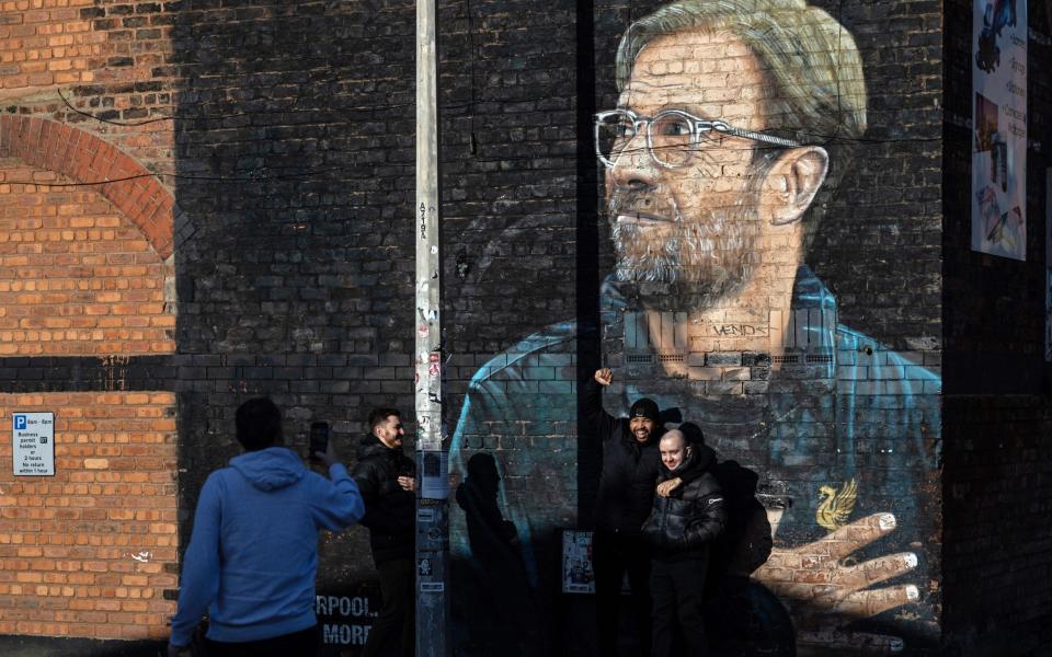 People pose for photographs next to a mural of Liverpool manager Jurgen Klopp