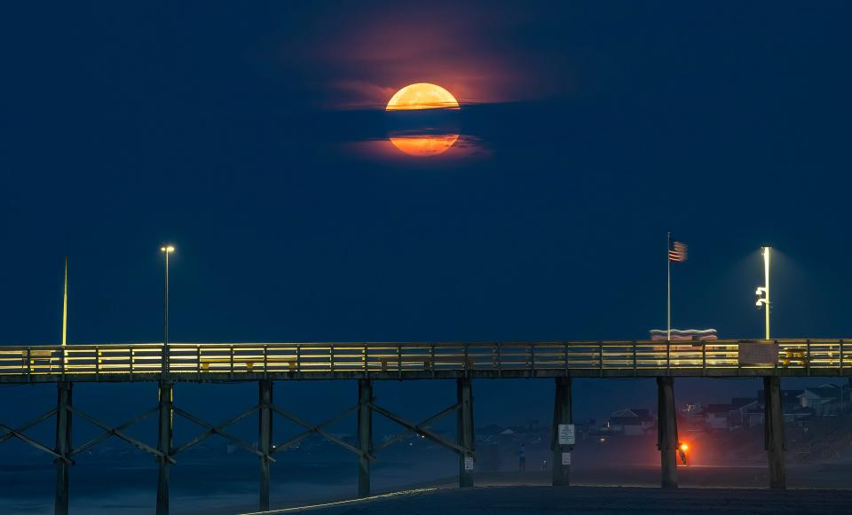 The full "super moon" is partially obscured by clouds as it sets above the Surf City Fishing Pier on the morning of July 3.  August brings two so-called super moons in the same calendar month, the second of which is dubbed a "blue moon."