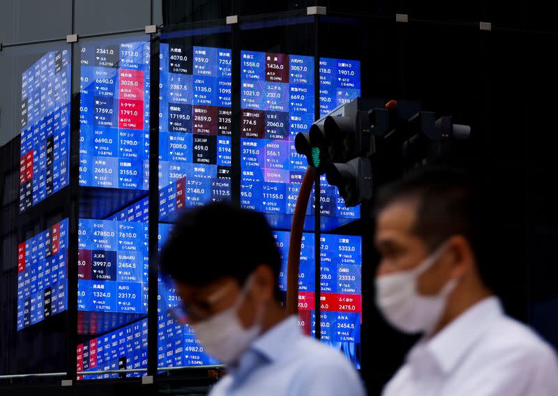 FILE PHOTO: People pass by an electronic screen showing Japan's Nikkei share price index inside a conference hall in Tokyo