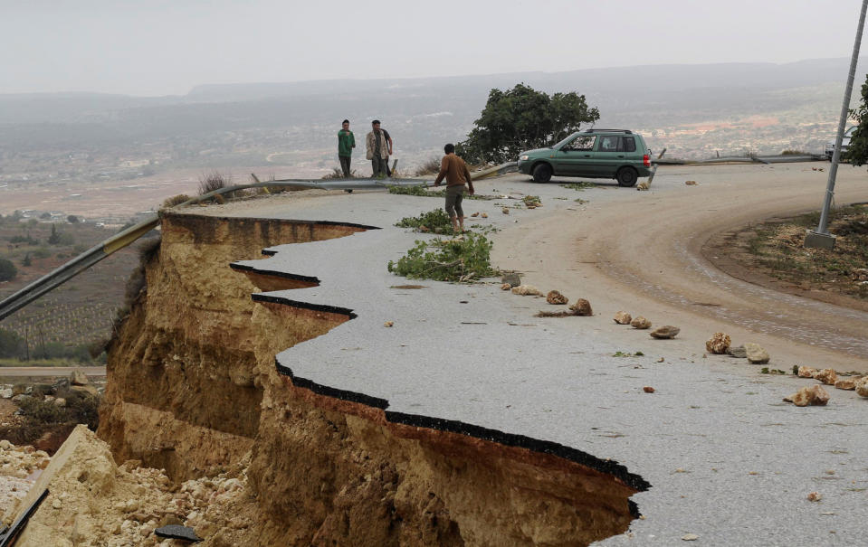 People stand along a road near where a storm has washed away part of the hillside.
