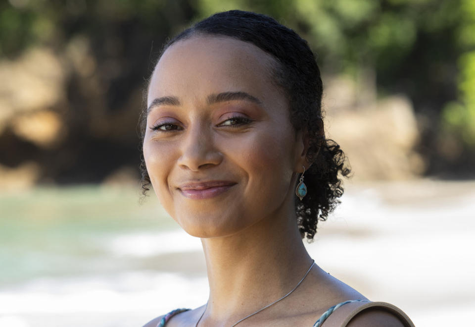 A generic shot of Chelsea Fielding (Emma Naomi) standing on the beach and smiling at the camera