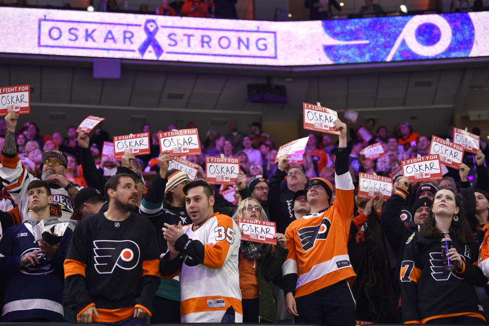 FILE - Fans hold signs in support of Philadelphia Flyers' Oskar Lindblom during a stoppage in the first period of an NHL hockey game against the Anaheim Ducks, Tuesday, Dec. 17, 2019, in Philadelphia. Philadelphia Flyers general manager Chuck Fletcher made what he called “a very difficult decision” in placing forward Oskar Lindblom on waivers on Tuesday, July 12, 2022, for the purpose of buying out the final year of his contract. As part of the decision to free up salary cap space in cutting a player who overcame being diagnosed with Ewing’s sarcoma, the Flyers are donating $100,000 to a Philadelphia organization supporting families impacted by cancer in Lindblom’s name. (AP Photo/Derik Hamilton, File)