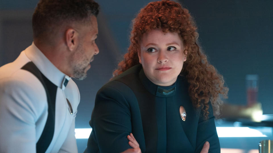 a woman with curly hair looks at a man in a white spacesuit