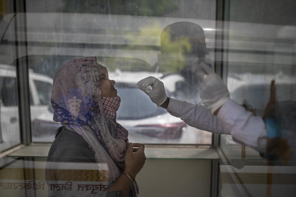 A health worker takes a swab sample to test for COVID-19 at a government hospital in Noida, a suburb of New Delhi, India, Wednesday, April 7, 2021. India hits another new peak with 115,736 coronavirus cases reported in the past 24 hours with New Delhi, Mumbai and dozens of other cities imposing night curfews to check the soaring infections. (AP Photo/Altaf Qadri)