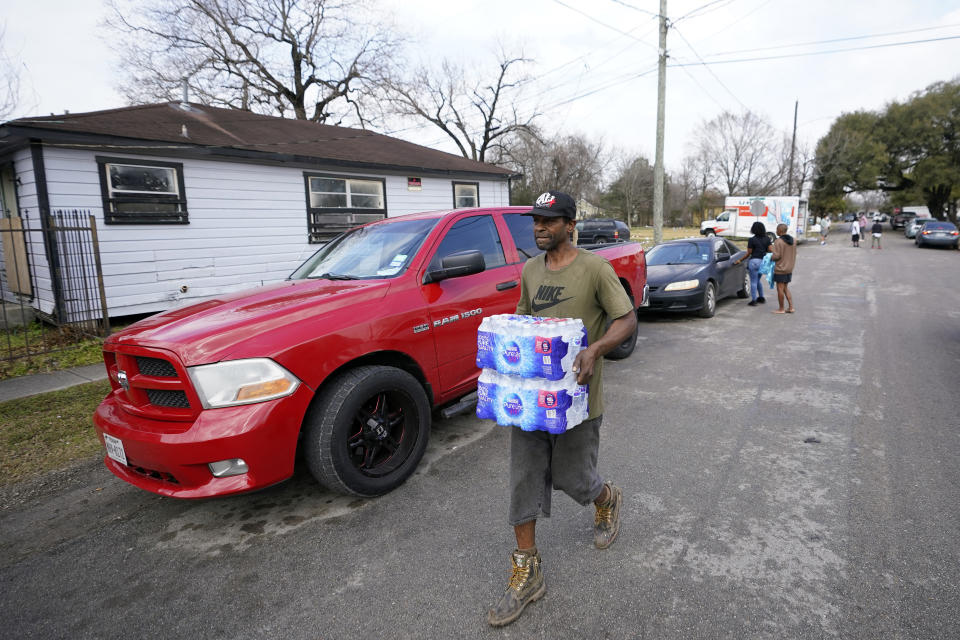 Ernest Collins carries cases of water back to his home, which was without running water for days after a recent winter storm, Friday, Feb. 26, 2021, in Houston. Local officials, including Houston Mayor Sylvester Turner, say they have focused their efforts during the different disasters on helping the underserved and under-resourced but that their work is far from complete. (AP Photo/David J. Phillip)