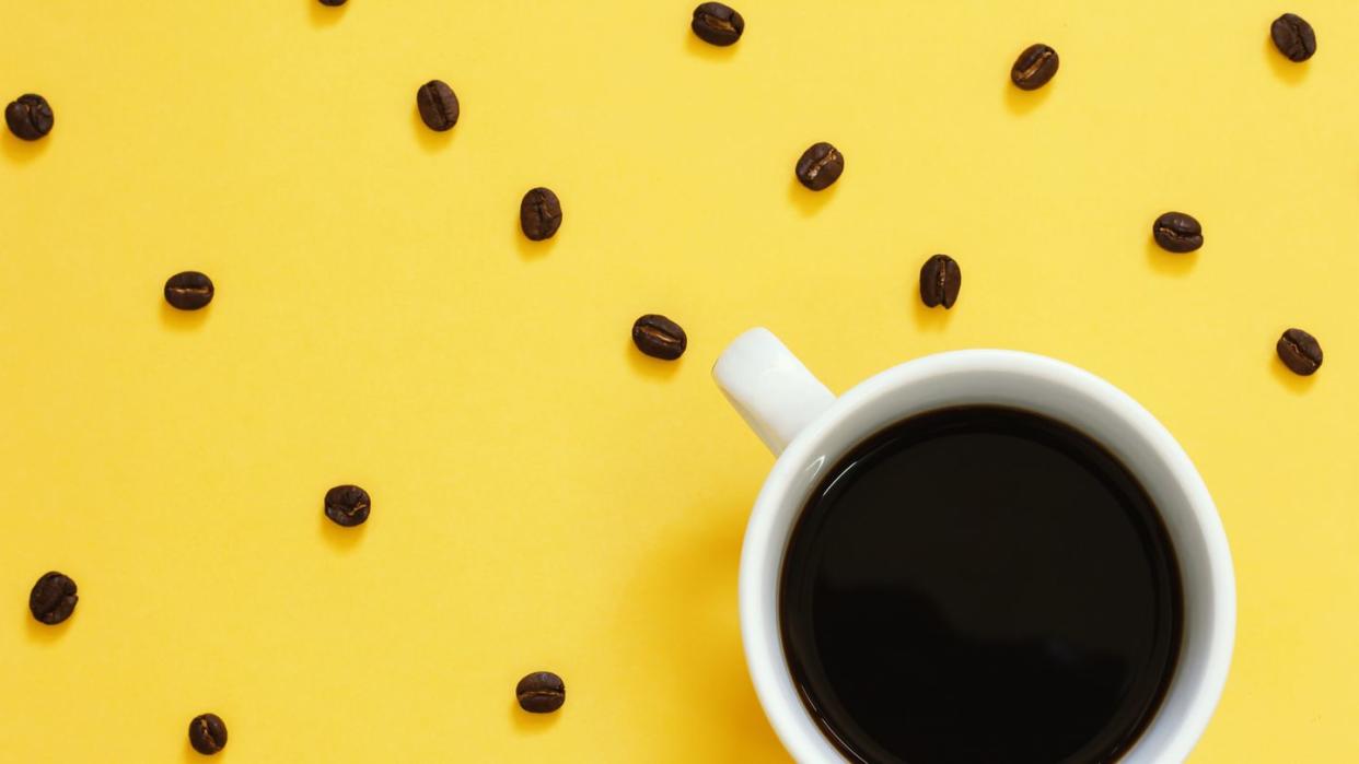 Top view of black coffee and beans on yellow background