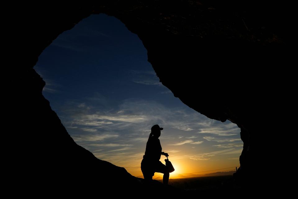 A hiker walks past the Hole-in-the-Rock at Papago Park during sunrise July 17, 2023, in Phoenix. Scientists say by far the biggest cause of the recent extreme warming is human-caused climate change and a natural El Nino. But some say there’s got to be something more.