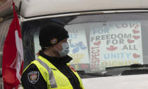 A police officer walks among protest vehicles as he distributes notices to protesters, Wednesday, Feb. 16, 2022 in Ottawa. Ottawa’s police chief was ousted Tuesday amid criticism of his inaction against the trucker protests that have paralyzed Canada's capital for over two weeks, while the number of blockades maintained by demonstrators at the U.S. border dropped to just one. (Adrian Wyld /The Canadian Press via AP)