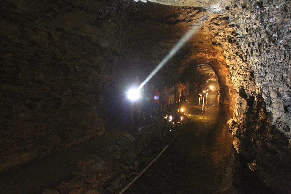 Tour Guide Kyle Burkwit leads a group on a tour of the Lockport Caves in Lockport, N.Y., on Aug. 21, 2014. A boat carrying hospitality workers capsized Monday, June 12, 2023, during a tour of the historic underground cavern system built to carry water from the Erie Canal beneath the western New York city of Lockport, killing one person who became trapped beneath the overturned vessel, officials said. (Mark Mulville/The Buffalo News via AP)