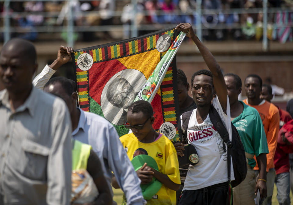 Members of the public carry a banner of former president Robert Mugabe as arrive to view his body as it lies in state at the Rufaro stadium in the capital Harare, Zimbabwe Friday, Sept. 13, 2019. The ongoing uncertainty of the burial of Mugabe, who died last week in Singapore at the age of 95, has eclipsed the elaborate plans for Zimbabweans to pay their respects to the former guerrilla leader at several historic sites. (AP Photo/Ben Curtis)