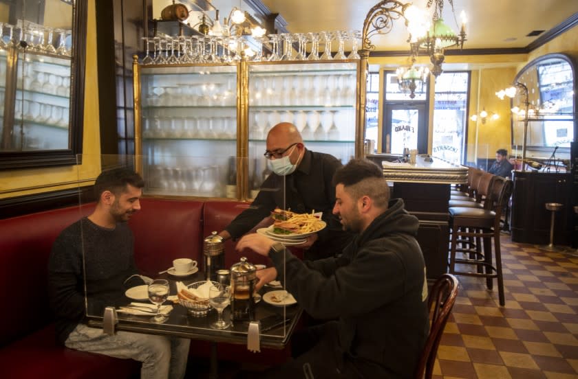 LOS ANGELES, CA - MARCH 15, 2021: Waiter Victor Alejo serves customers indoors for the first time since the coronavirus pandemic at Figaro Bistro on March 15, 2021 in Los Angeles, California. The restaurant spread out the indoor seating and installed plexiglass at each table.(Gina Ferazzi / Los Angeles Times)