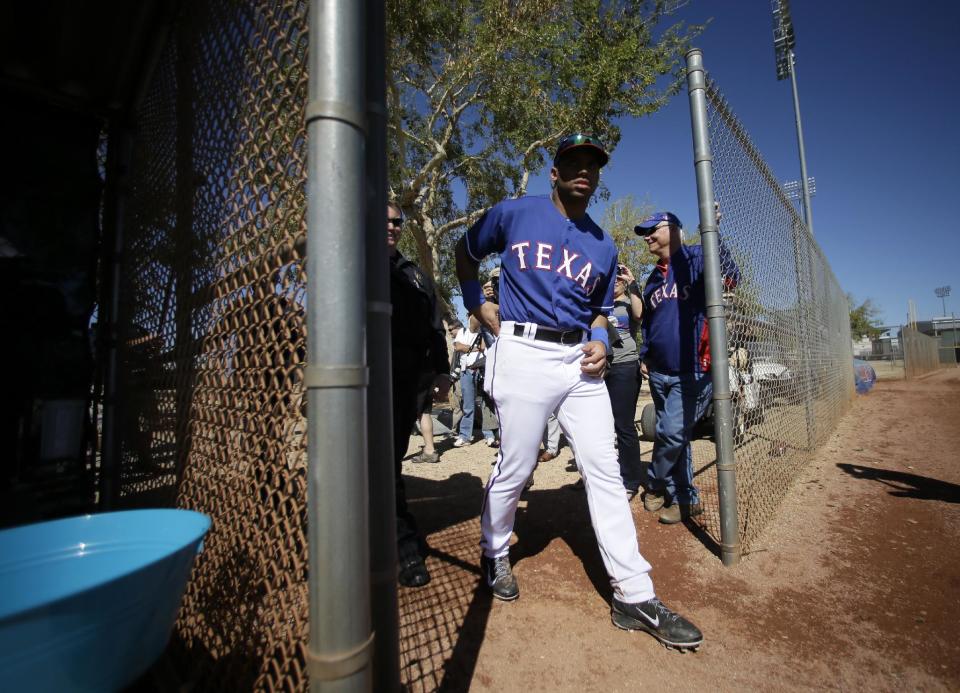 Seattle Seahawks quarterback Russell Wilson walks on to the practice field after signing autographs during spring training baseball practice with the Texas Rangers, Monday, March 3, 2014, in Surprise, Ariz. (AP Photo/Tony Gutierrez)