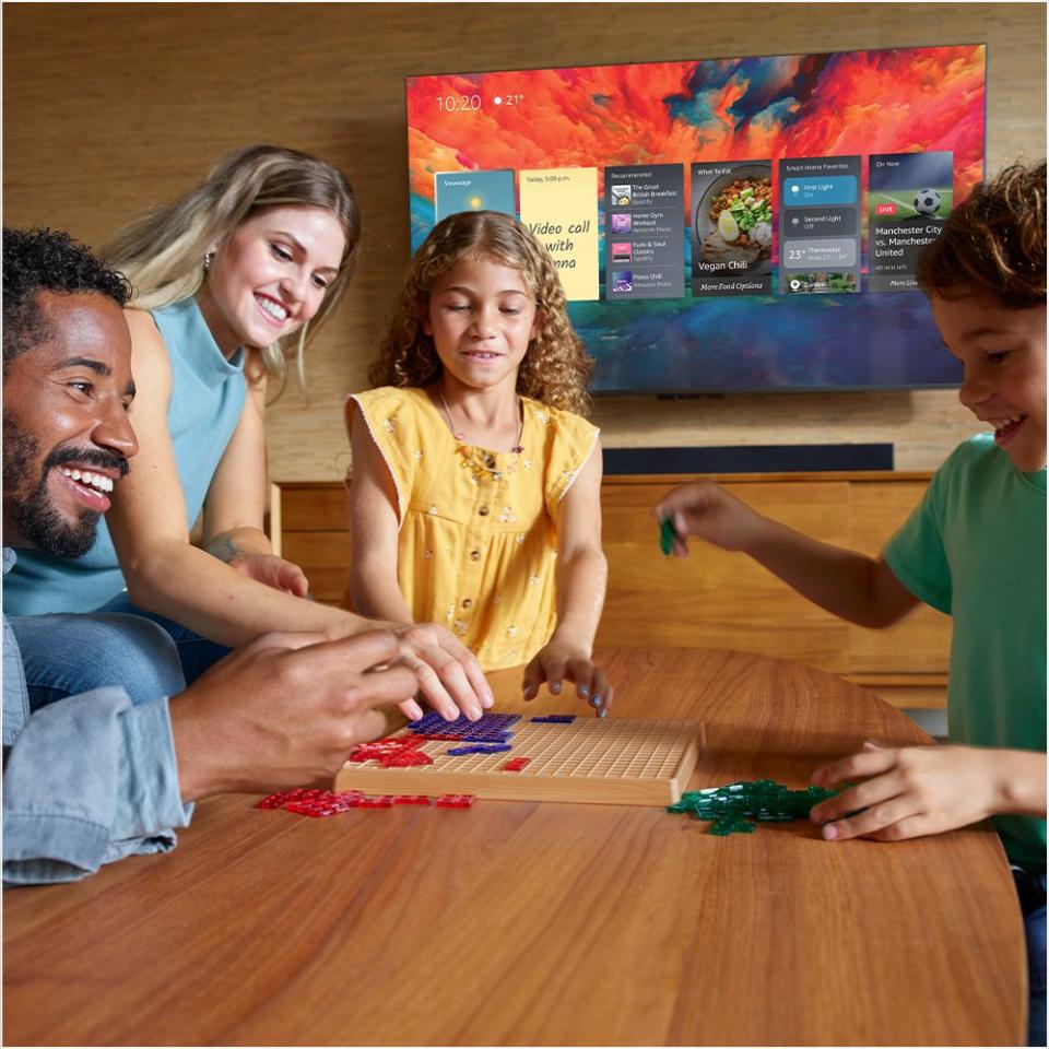 amazon fire omni qled tv on the wall behind a family playing games