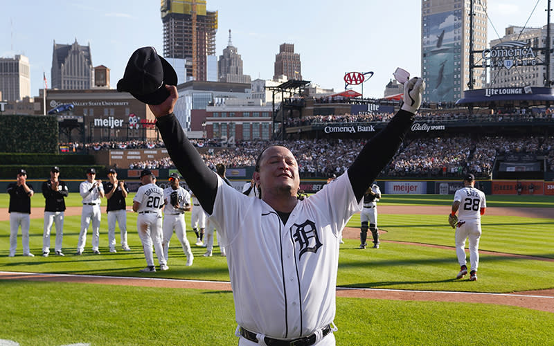 Detroit Tigers' Miguel Cabrera raises his arms toward the crowd. Behind him, team members on the baseball field applaud, and in the distance are stands crowded with fans.