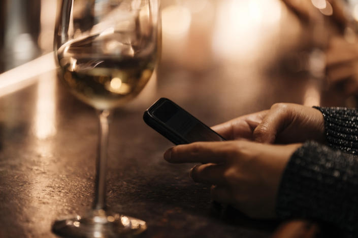 A woman sits at a bar with wine and her phone