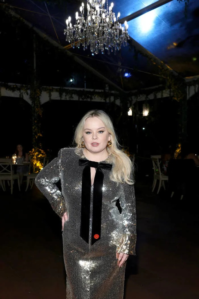 Nicola Coughlan on the red carpet in a long-sleeve, sparkling dress with a lack ribbon tie wearing the pin