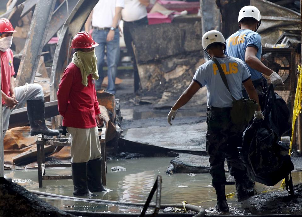 Workers look as police carry a body bag containing a charred remains of a worker inside a gutted slipper factory in Valenzuela