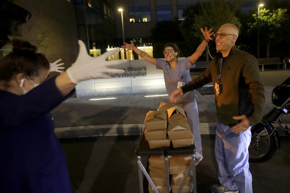 Nightbird Restaurant chef and owner Kim Alter, left, mimics giving a hug to nurse practitioner Sydney Gressel, center, and patient care technician Matt Phillips after delivering dinner to them at University of California at San Francisco Benioff Children's Hospital in San Francisco, March 27, 2020. A group of tech-savvy, entrepreneurial San Francisco friends wanted to help two groups devastated by the coronavirus pandemic. They came up with a plan that involved soliciting donations, tapping friends in the restaurant world and getting San Francisco hospitals to accept free food cooked up by some of the city's top chefs. (AP Photo/Jeff Chiu)