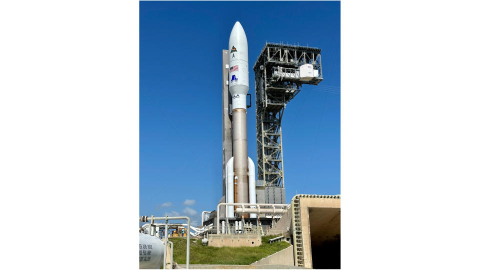 a brown and white rocket sits next to a large metallic tower with blue sky in the background.