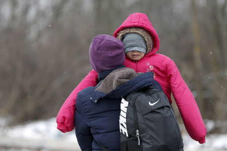 A migrant carries a child as they walk through a frozen field after crossing the border from Macedonia, near the village of Miratovac, Serbia, January 18, 2016. REUTERS/Marko Djurica