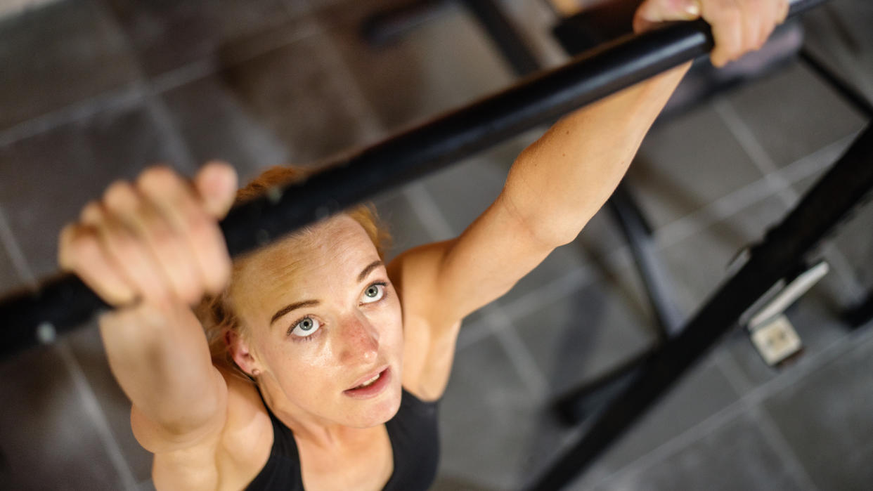  Woman gripping pull-up bar and looking up at it. 